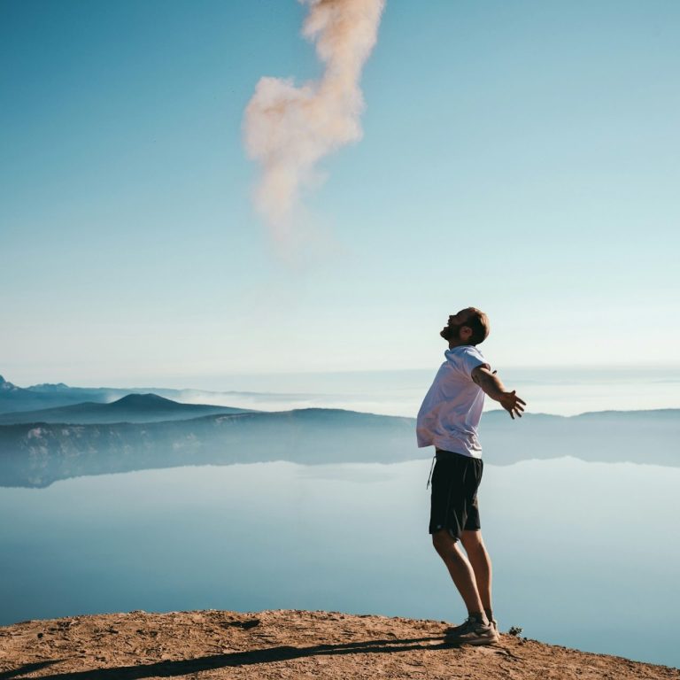 Mann steht auf einem Felsen, breitet die Arme aus und schaut zum Himmel.