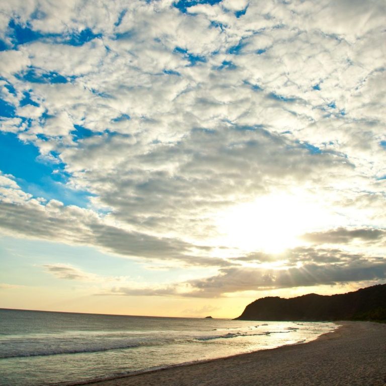 Sonnenuntergang über einem ruhigen Strand mit angenehm bewölktem Himmel.